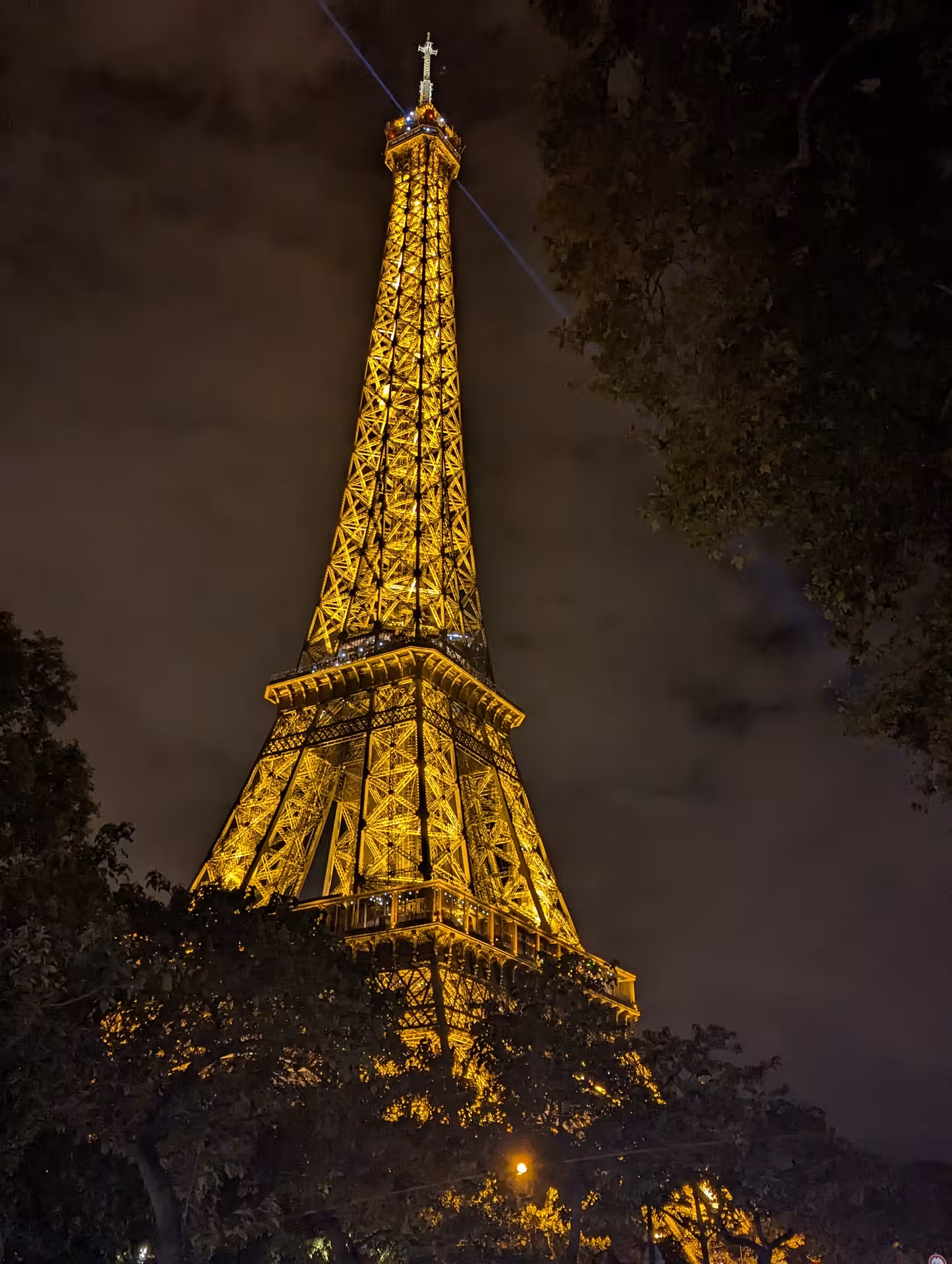 Eiffel Tower illuminated in golden lights at night with searchlight beam from summit, Paris