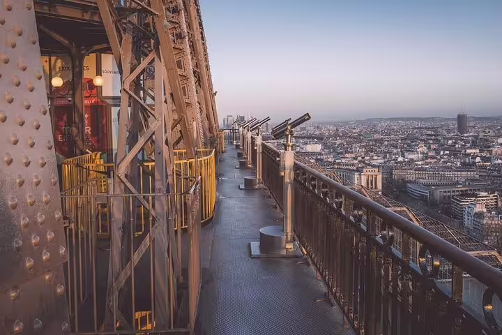 Observation deck of the Eiffel Tower with coin-operated telescopes overlooking the Paris city skyline at dusk