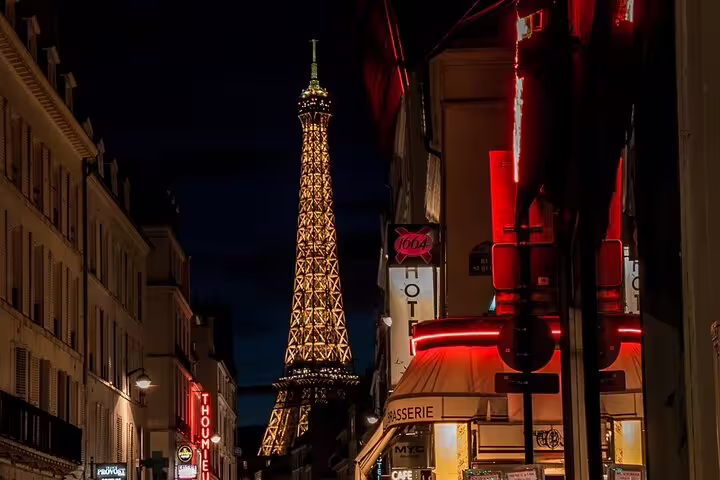 Eiffel Tower illuminated at night viewed from a Parisian street with neon-lit cafes and brasseries
