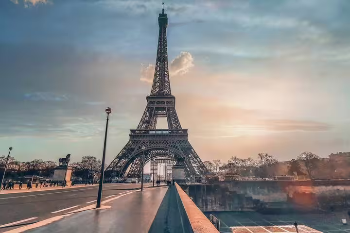 Eiffel Tower at sunset viewed from a bridge in Paris with visitors walking nearby
