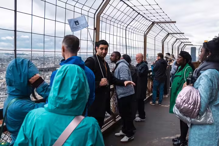 Tour guide leading a group of tourists on the Eiffel Tower top floor observation deck with Paris skyline views