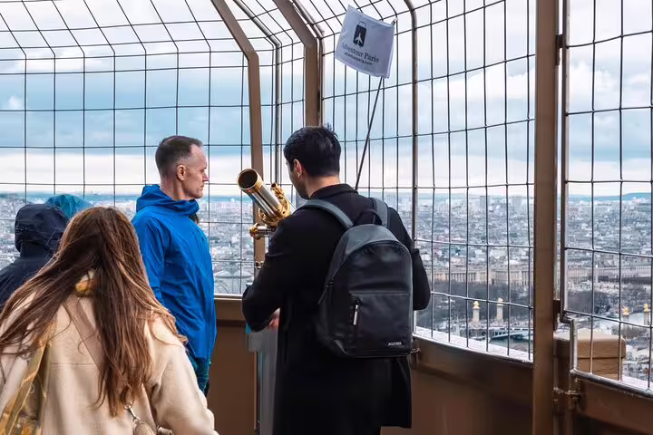 Tourists using a coin-operated telescope on the Eiffel Tower top floor with panoramic views of Paris