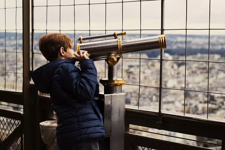 Child looking through coin-operated binoculars at Paris cityscape from Eiffel Tower top floor observation deck