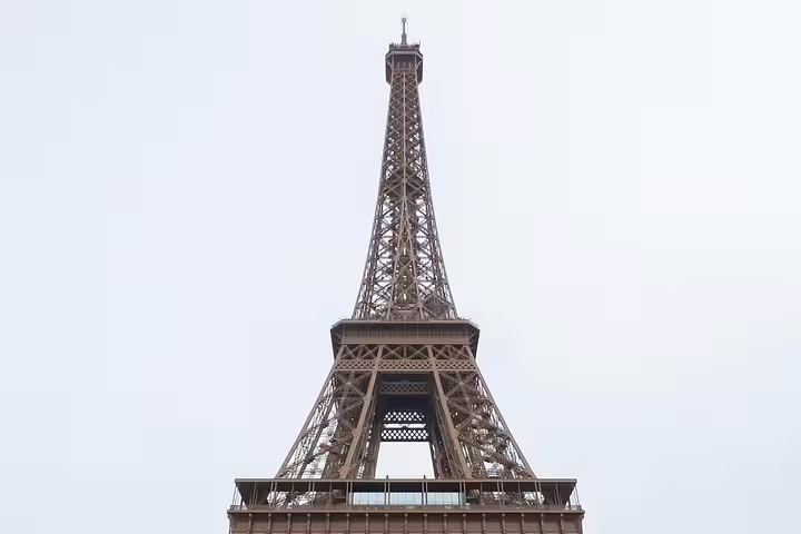 View looking up at the Eiffel Tower's iron lattice structure against a pale sky, Paris