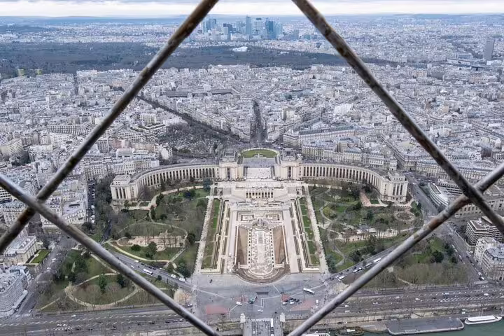 Aerial view of Trocadéro gardens and Paris skyline seen through Eiffel Tower iron lattice from top floor