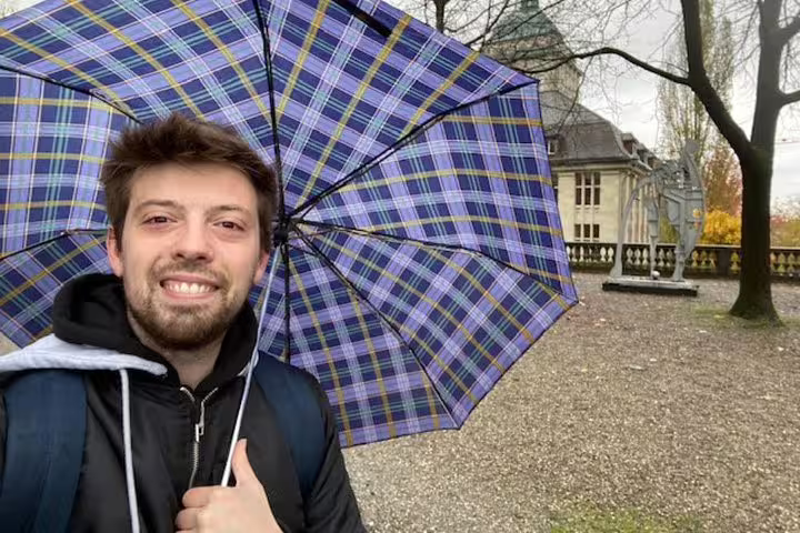 Smiling man holding plaid umbrella on Einstein walking tour in Zurich on a rainy day
