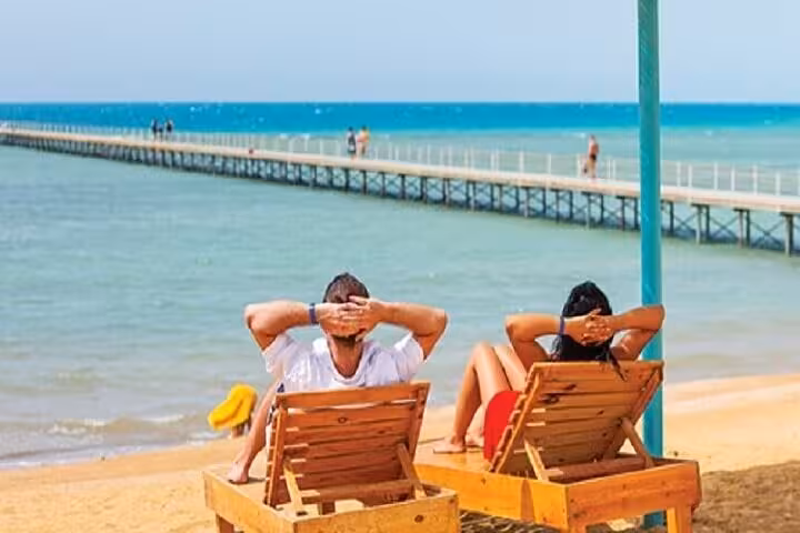 Couple relaxing on beach loungers by the Red Sea during El Ain El Sokhna day trip from Cairo with pier view