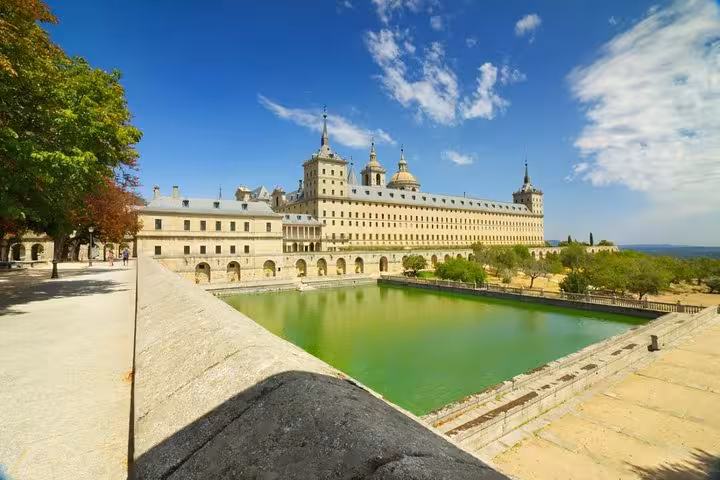 Stunning view of El Escorial Monastery with its reflecting pond and lush surroundings on a scenic day tour from Madrid.