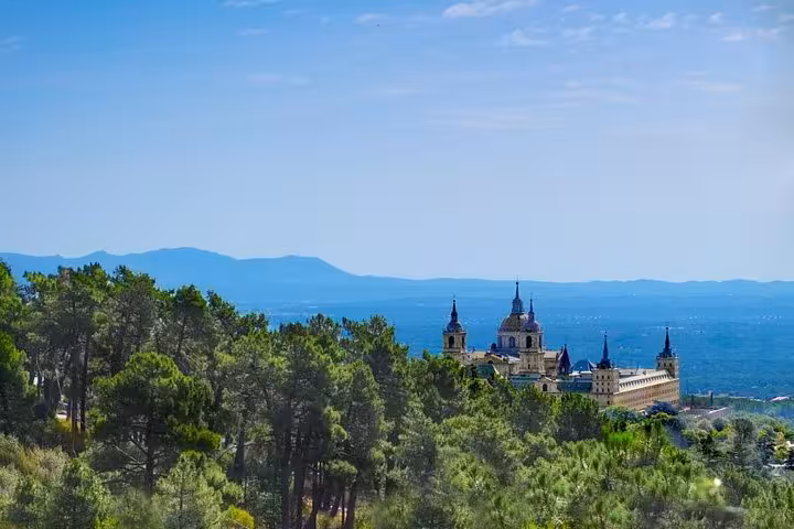 Scenic view of El Escorial Monastery surrounded by lush greenery on a clear day, featured in the Madrid day tour.