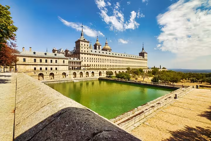 Experience the grand architecture of El Escorial with its reflective pond, nestled in a scenic landscape near Madrid.