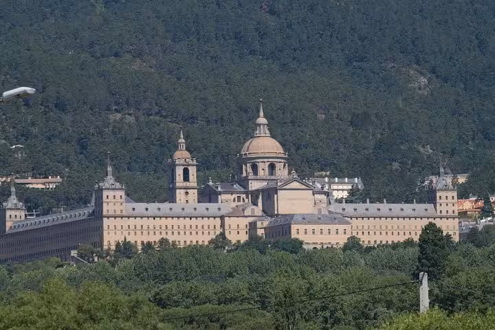 Panoramic view of El Escorial nestled in lush greenery, showcasing its majestic structure on a half-day tour from Madrid.