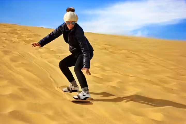 Traveler sandboarding on golden dunes in El Fayoum Oasis desert, part of overnight camping trip from Cairo