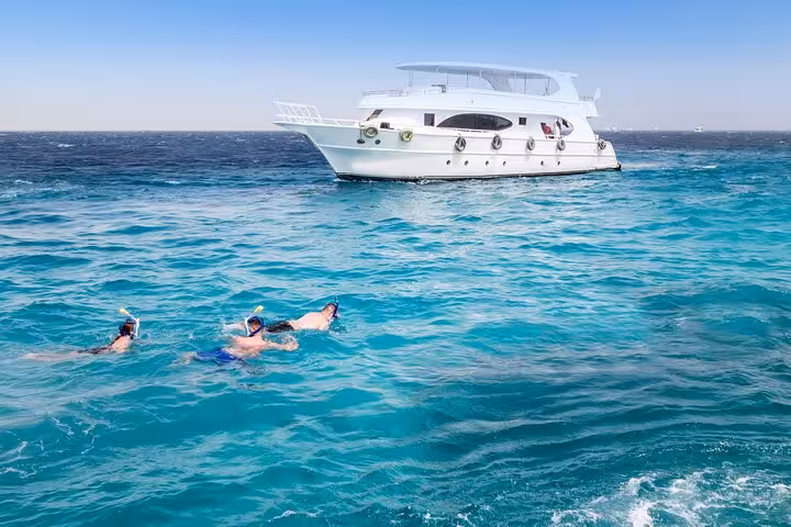 Snorkelers in turquoise Red Sea near yacht in El Gouna Lagoon, dolphin snorkeling tour with onboard lunch