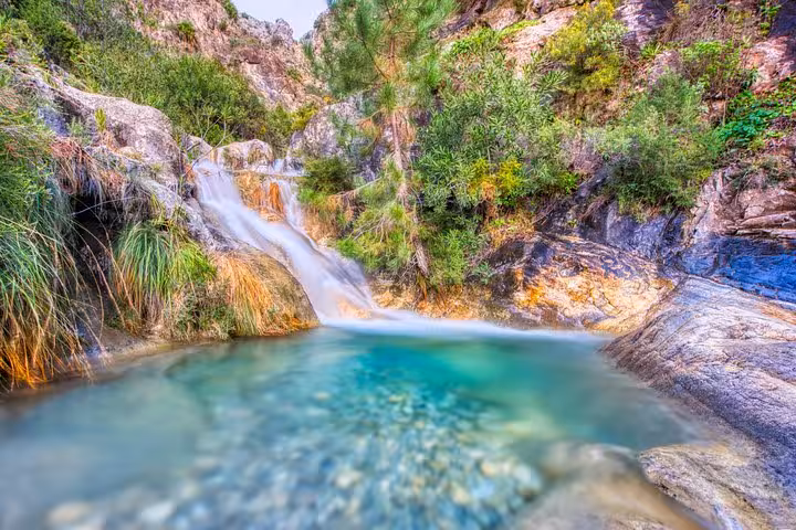 Crystal-clear waterfall flowing into a turquoise pool surrounded by rocks and greenery on El Saltillo hiking tour.