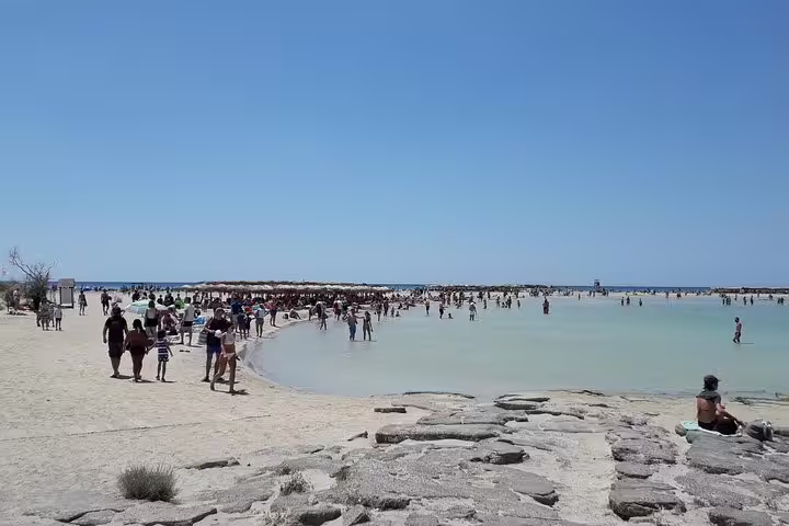 Tourists enjoy the crystal-clear waters and stunning pink sand at Elafonisi Beach during a private tour from Chania.