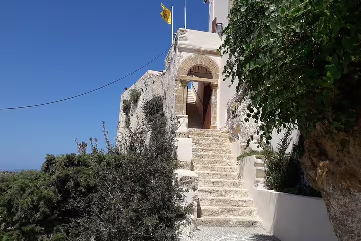 Stone staircase leading to a historic building with flags, surrounded by lush greenery near Elafonissi Beach.