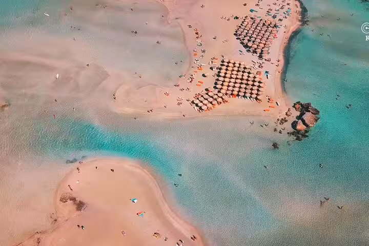 Aerial view of Elafonissi Beach lagoon with pink sand and umbrellas on a day trip from Rethimno, Crete