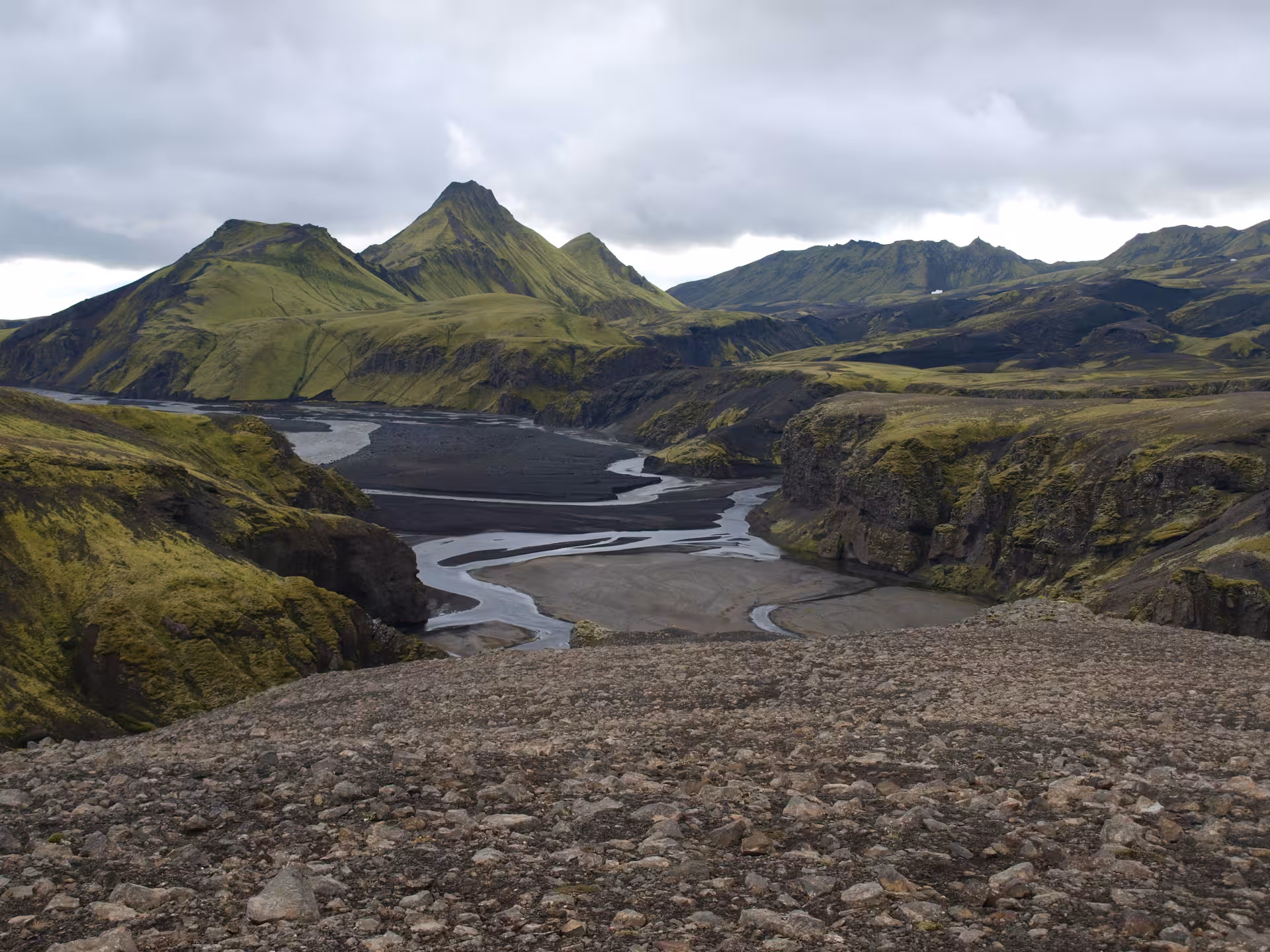 Braided glacial river winding through black volcanic canyon with green moss-covered mountains in Iceland