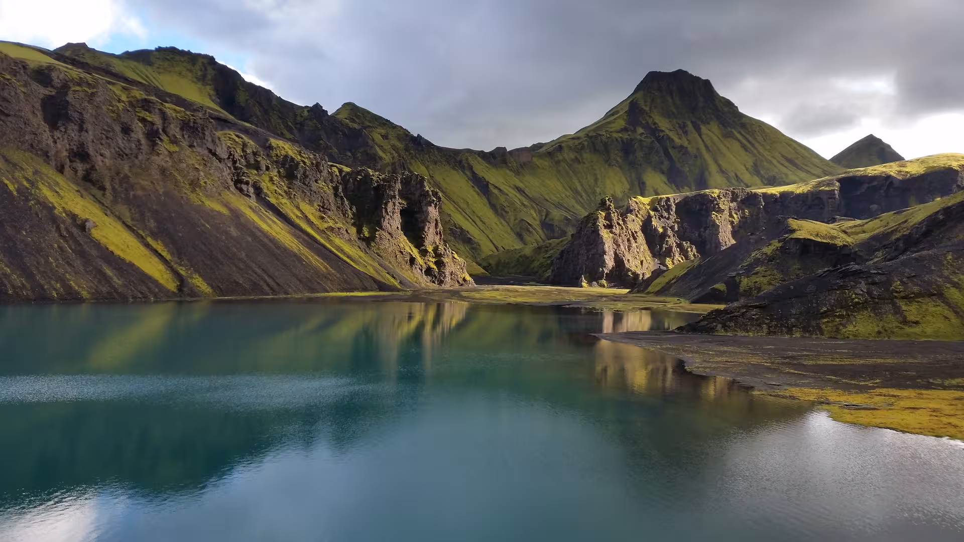 Turquoise glacial lake reflecting moss-covered volcanic mountains in Eldgja Canyon, Iceland Highlands