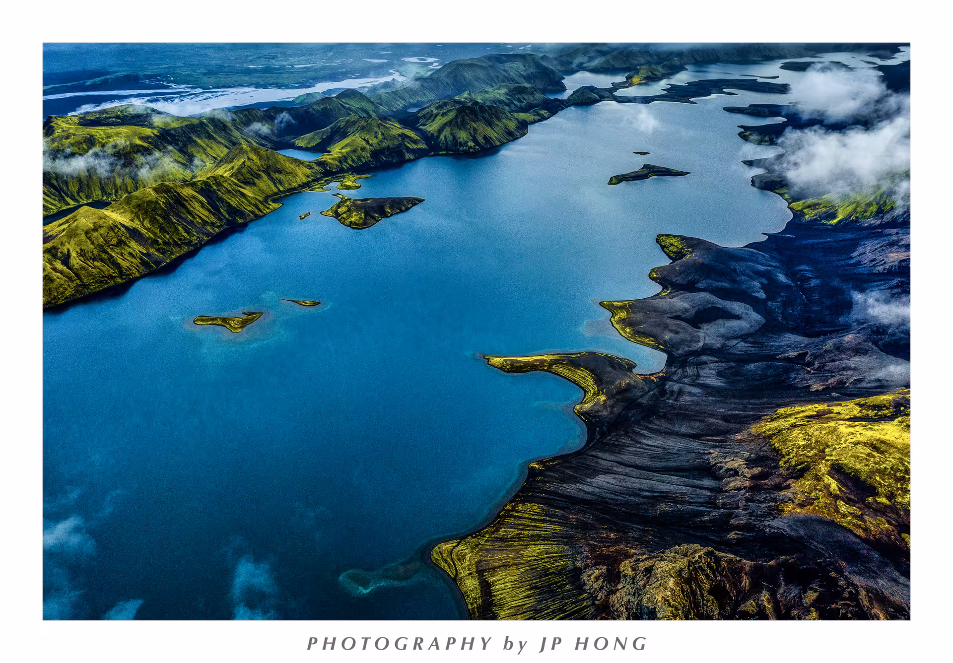 Aerial view of vivid blue glacial lake with volcanic black lava fields and green moss-covered highlands, Iceland