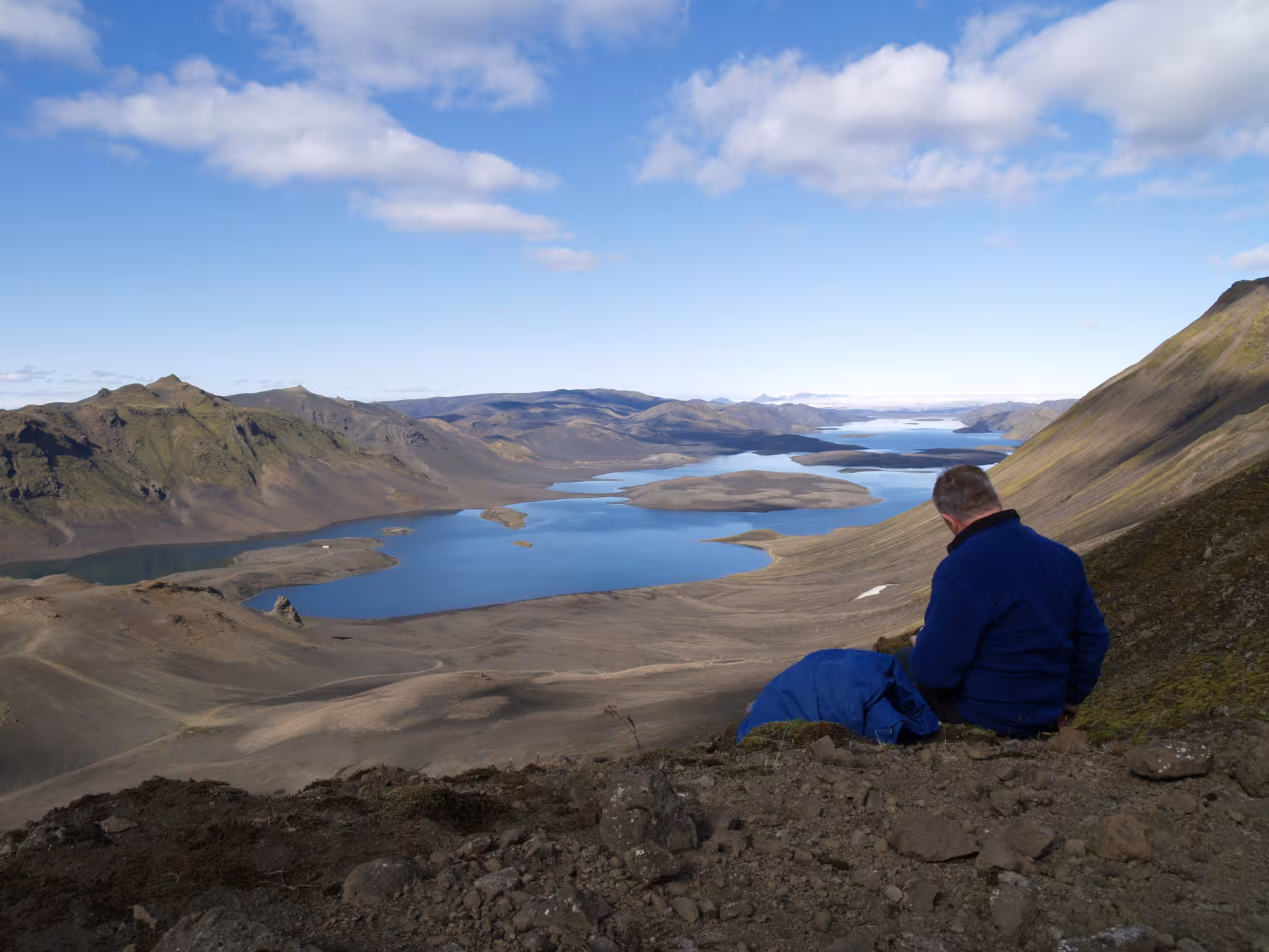 Hiker resting on hillside overlooking vast blue glacial lake and volcanic landscape in Iceland