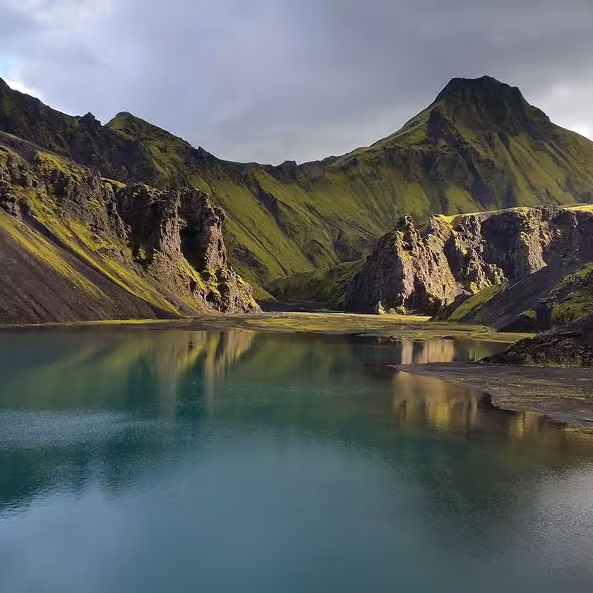 Turquoise glacial lake reflecting moss-covered volcanic mountains in Eldgja Canyon, Iceland