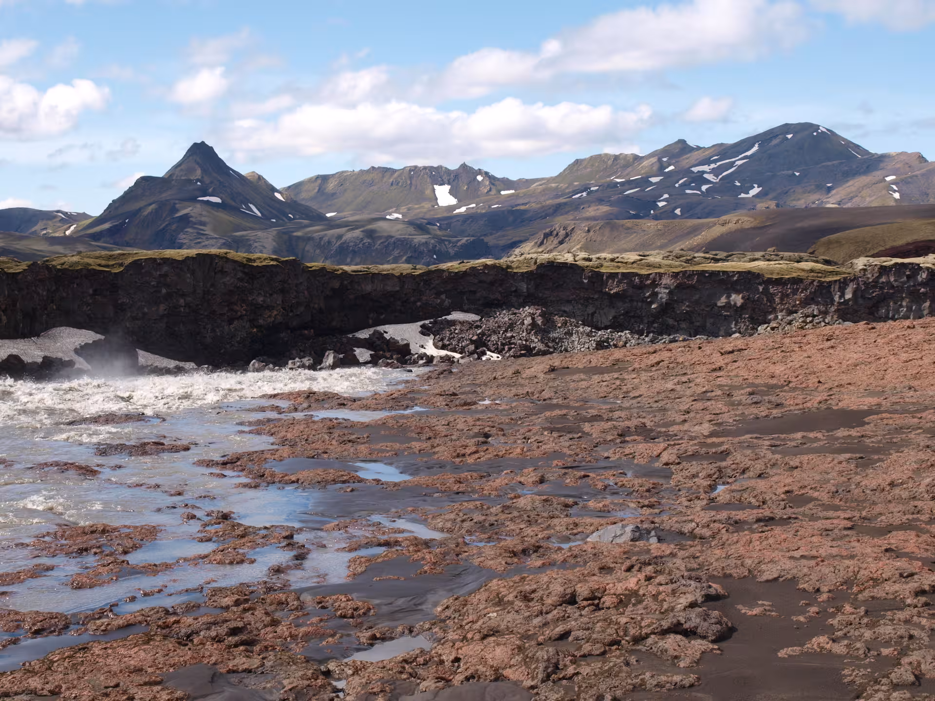 Red volcanic lava field with rushing river and snow-capped highlands mountains in Iceland