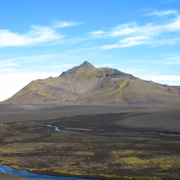 Volcanic mountain peak rising over dark lava plains with winding river, Eldgjá Canyon region, Iceland