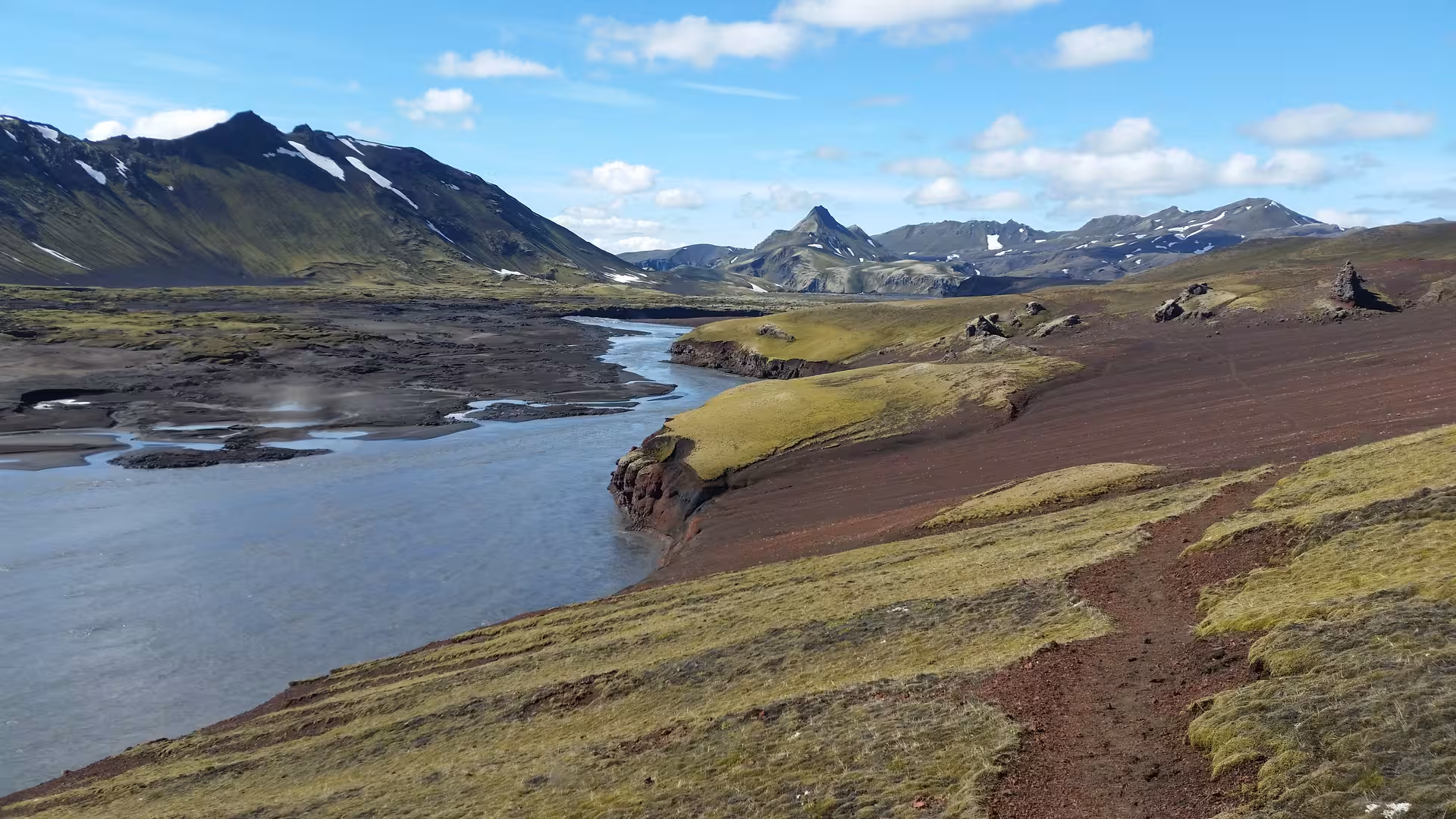Glacial river winding through red volcanic terrain with snow-capped mountains in Iceland's highlands