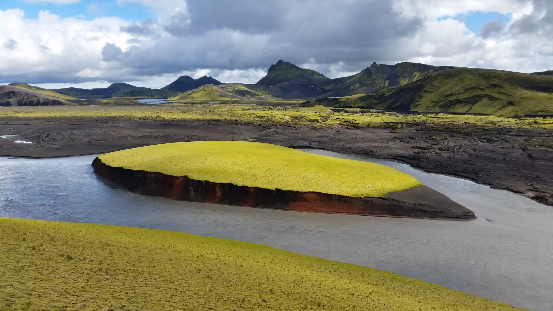 Moss-covered river island with red volcanic banks winding through Iceland's highland lava fields near Eldgja Canyon