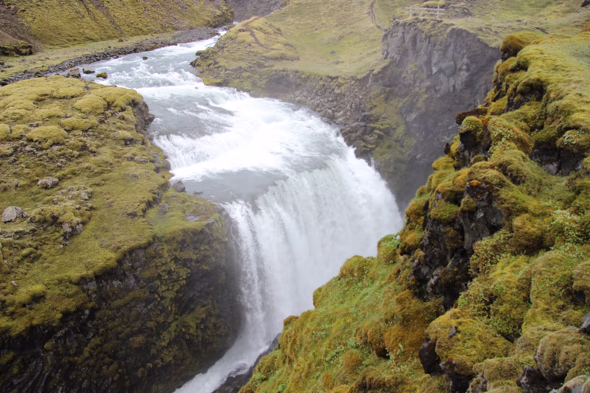 Rushing waterfall cascading over mossy lava rock cliffs along a river canyon in Iceland