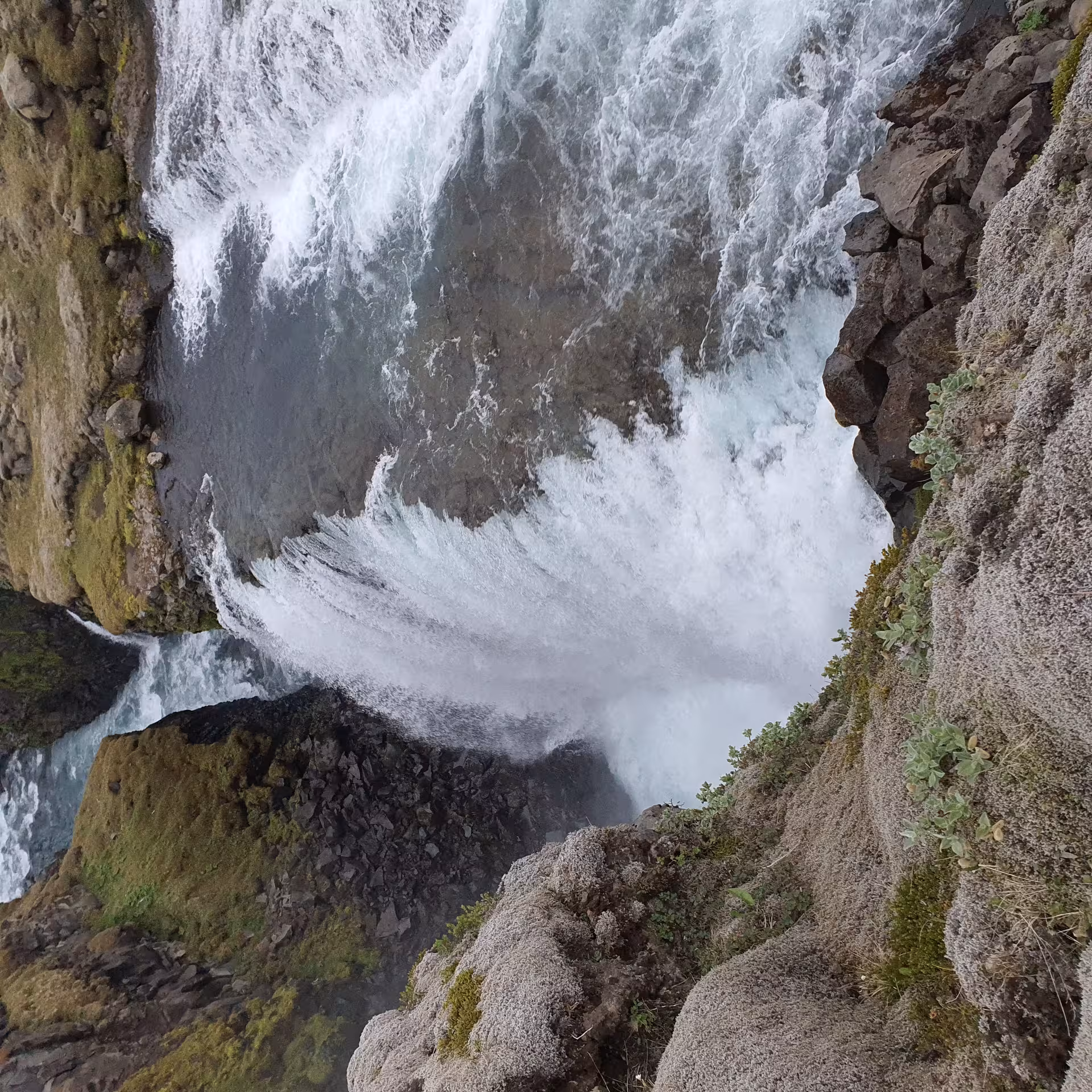 Looking down into a powerful waterfall cascading through a rocky volcanic canyon with mossy green walls