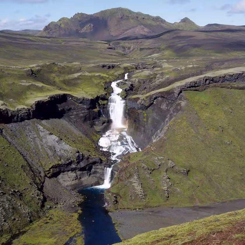 Aerial view of cascading waterfalls through Eldgjá volcanic canyon with green moss-covered highlands Iceland