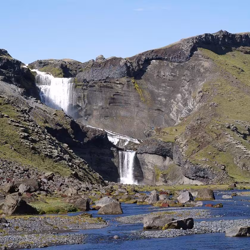 Eldgjá canyon waterfall cascading in two tiers into a rocky river with green volcanic hills in Iceland