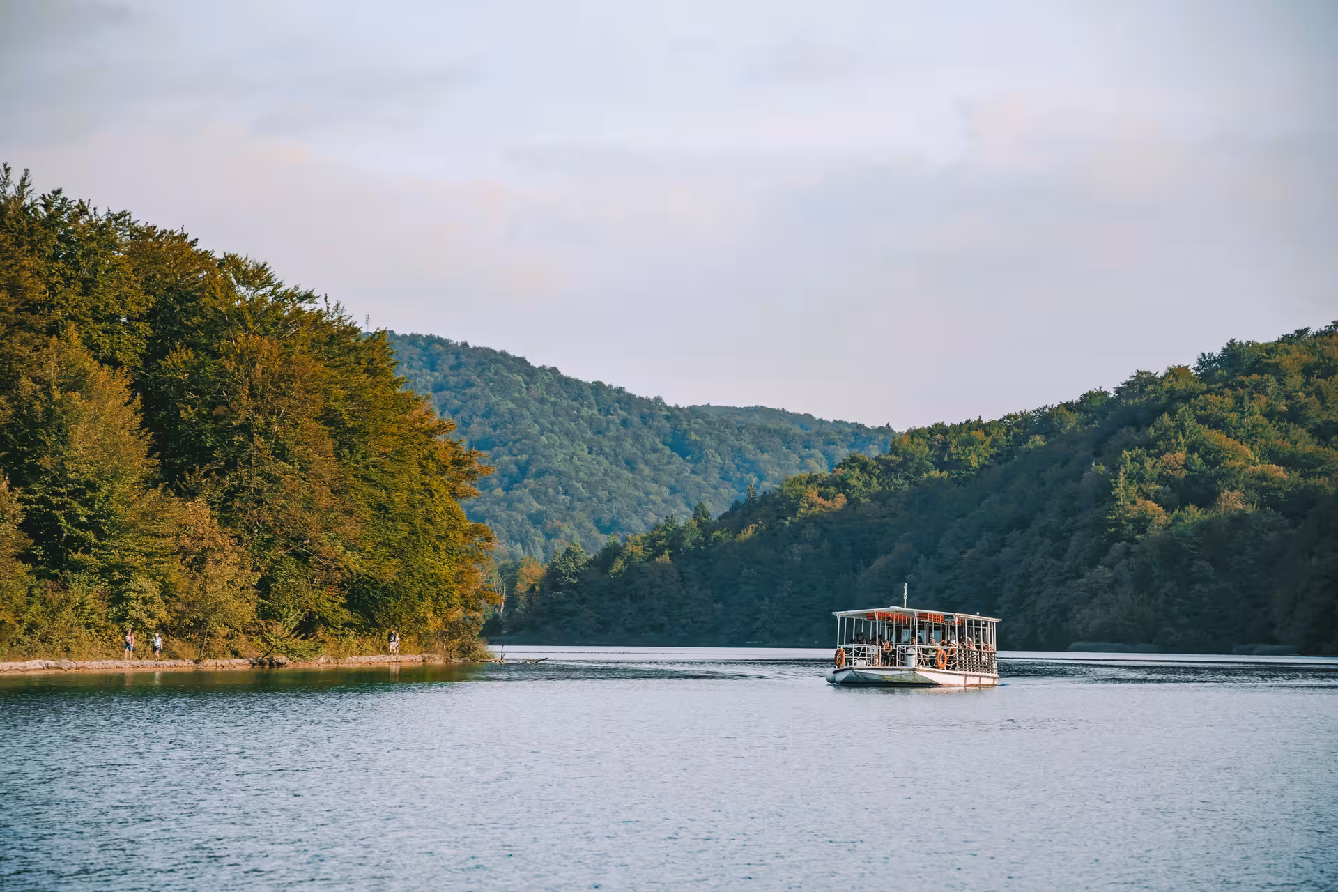 Electric boat crossing a calm Plitvice lake surrounded by green hills on the Plitvice Lakes tour from Zadar