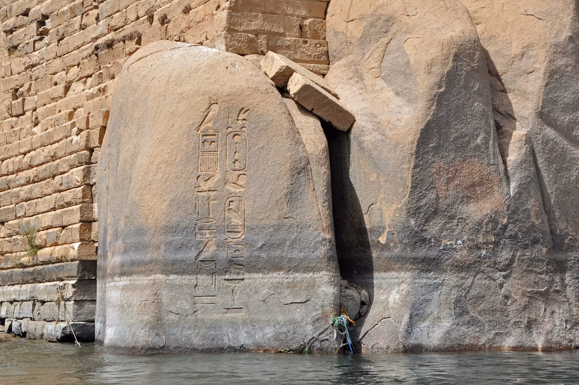 Ancient Egyptian hieroglyphic stele at Elephantine Island rising from Nile waters beside stone temple wall