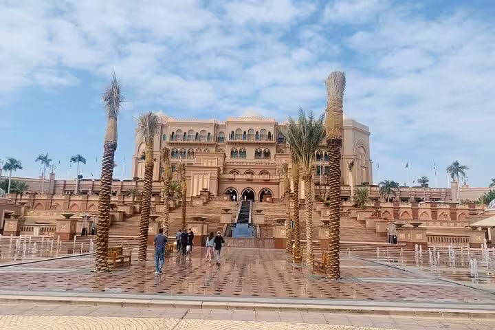 Tourists exploring Emirates Palace grand entrance with fountains and palm trees on Abu Dhabi city tour