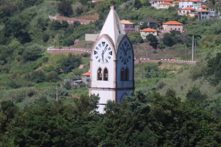 Scenic view of a church tower amidst lush vineyards and hillside homes on the Enchanted Vineyards 4x4 Wine Tour to Cabo Girão.