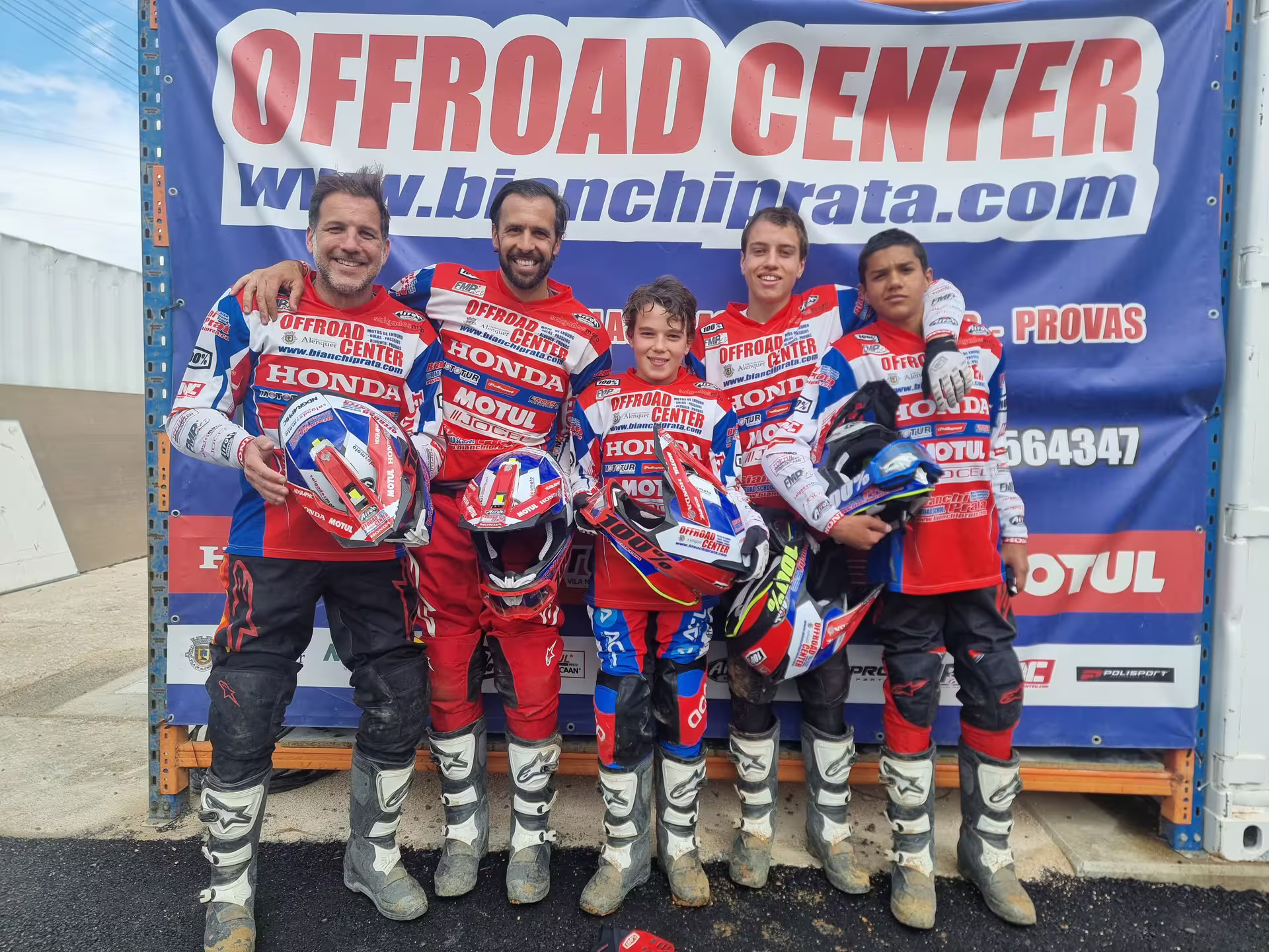 Smiling group of enduro riders in matching gear posing with helmets at Offroad Center in Carregado, Lisbon.