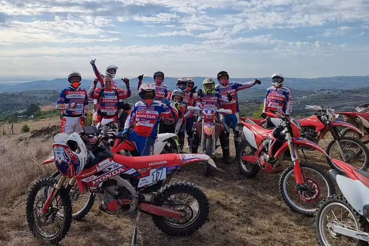 Excited enduro riders posing with bikes on a scenic Lisbon hilltop with panoramic views and clear skies.