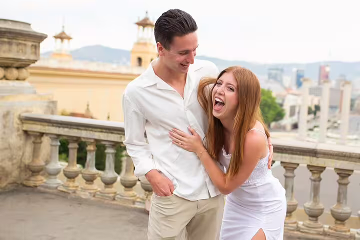 Happy couple laughing on Barcelona viewpoint terrace during engagement photo session with city skyline views