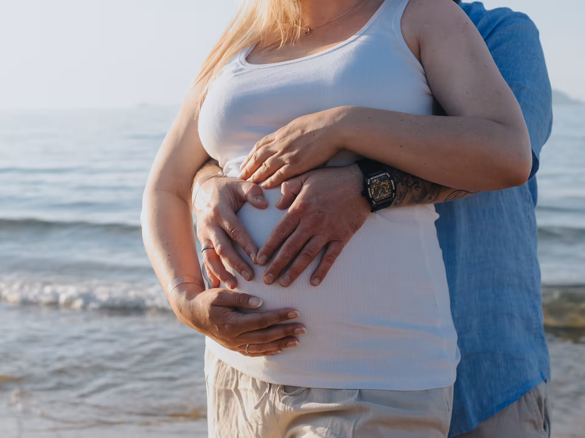 Close-up of couple's hands on a baby bump by the sea, celebrating love at Heraklion Venetian Port photoshoot.