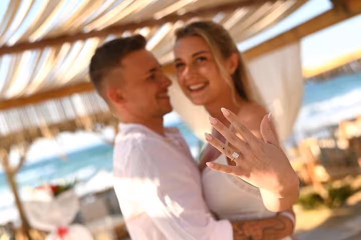 Happy couple celebrates engagement with a beachside photoshoot in Hersonissos, showcasing a sparkling ring.