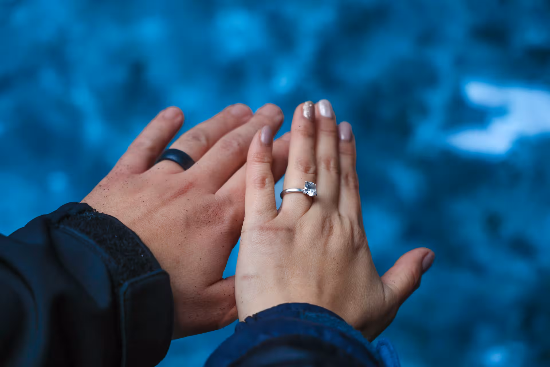 Close-up of couple's hands showing engagement ring against icy blue Iceland glacier lagoon backdrop on sunrise proposal tour
