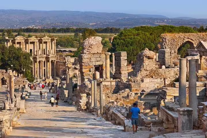 Tourists walking along the ancient marble streets of Ephesus with historic ruins and columns lining the pathway.