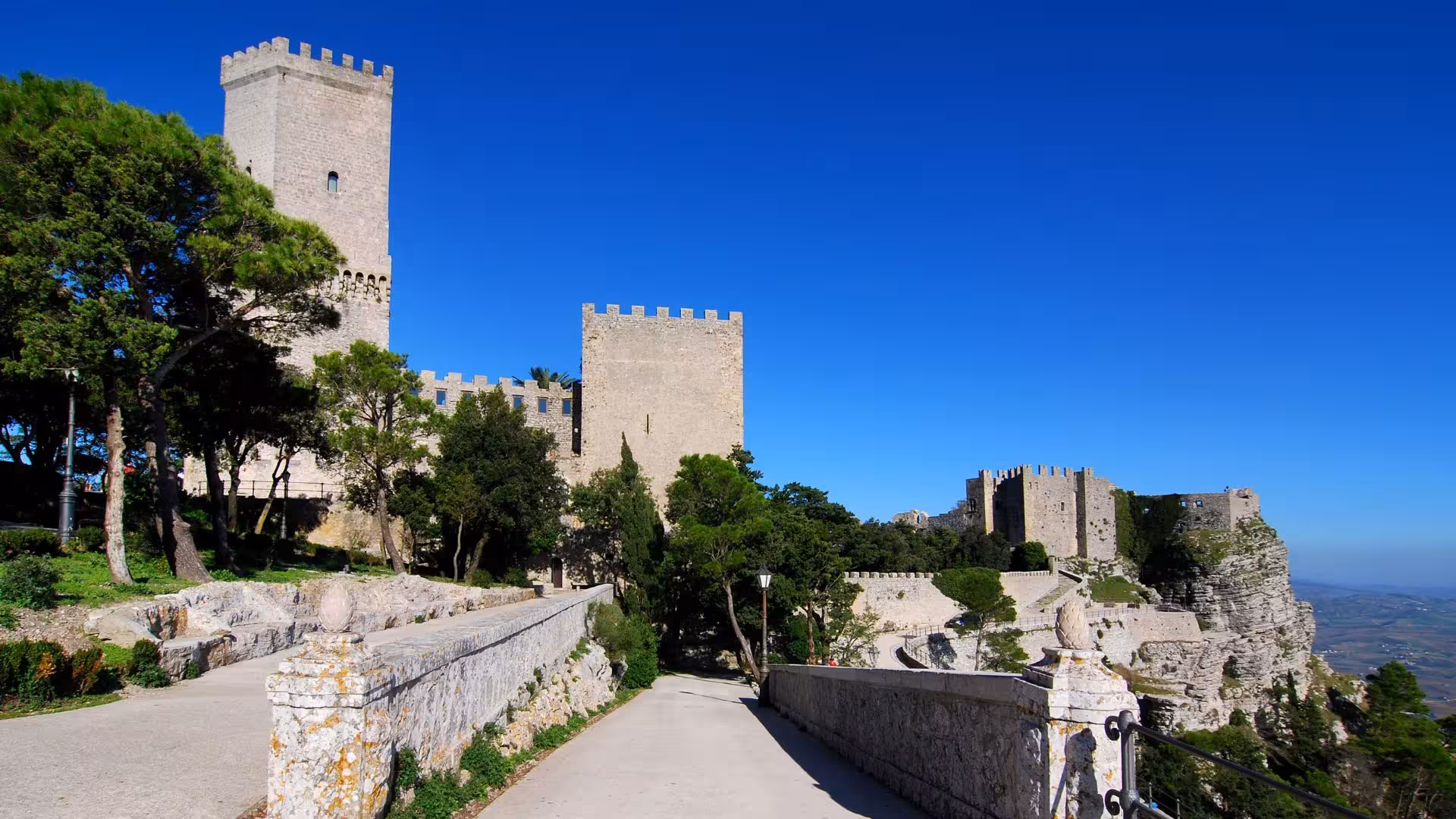 Historic Erice castle with stone towers and lush greenery under a clear blue sky, perfect for ebike tours.