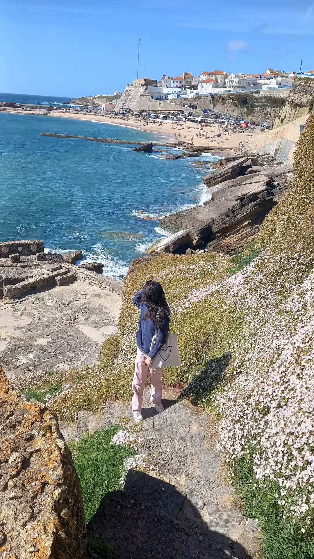 Tourist enjoying the scenic coastal path in Ericeira with vibrant flowers and ocean views.