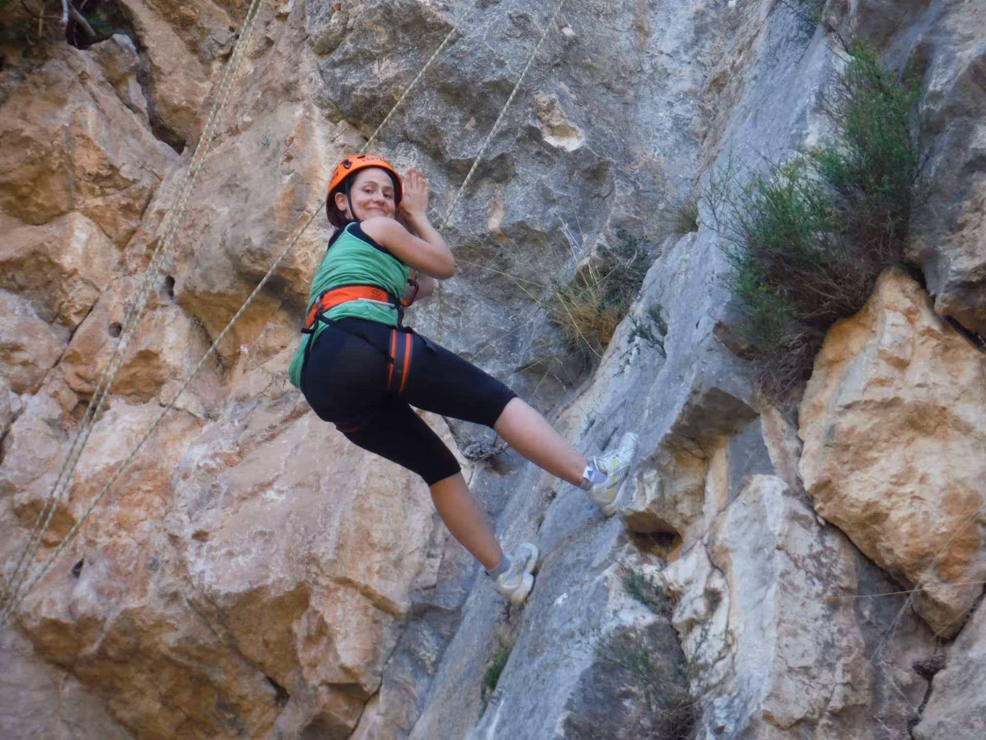 Participante sonriente en escalada para principiantes con casco y arnés, practicando técnica en roca con guía