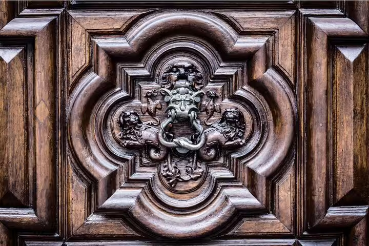 Ornate dark wooden door with bronze lion head door knocker and carved mythical creatures, Turin