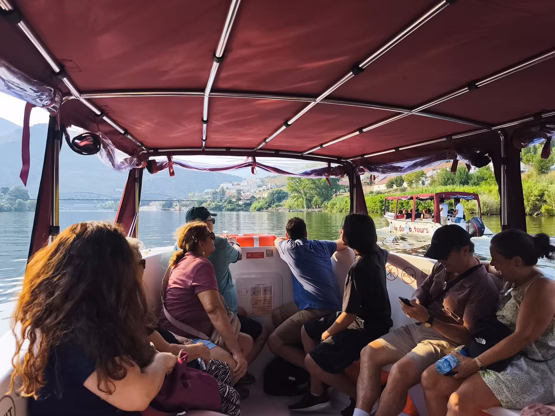 Essence Tour Douro River cruise with passengers under canopy, scenic vineyards and riverside villages in Portugal